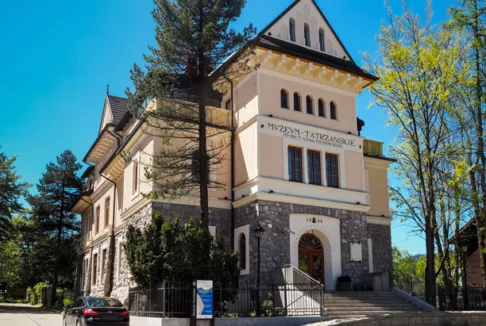 Muzeum Tatrzańskie im. Tytusa Chałubińskiego w Zakopanem (nowe zdjęcie): Nowoczesna fotografia muzeum, ukazująca odrestaurowany budynek w pełnym świetle słonecznym. Wokół budynku widać drzewa, a przed wejściem zaparkowany samochód.