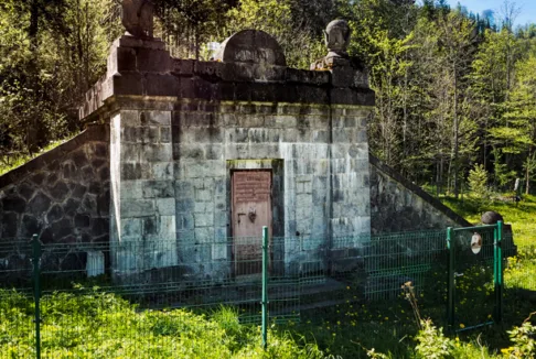 Zbiornik wody w Kuźnicach: Fotografia przedstawia kamienny zbiornik wody otoczony zielenią i drzewami, z metalowym ogrodzeniem wokół. Konstrukcja ma solidne kamienne ściany i schody po bokach.